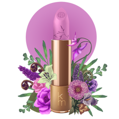 A natural lipstick in a gold-colored tube, labeled with 'KM' and a floral design, indicating a lilac color.